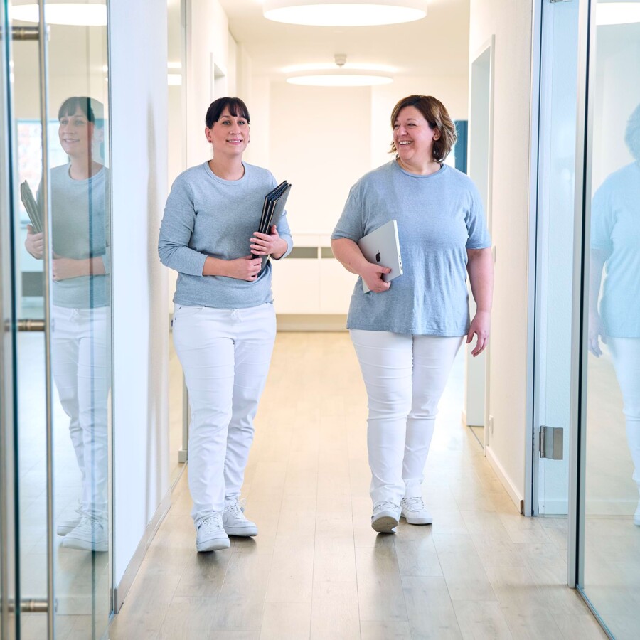 Zwei Mitarbeiterinnen laufen &uuml;ber den Praxisflur.