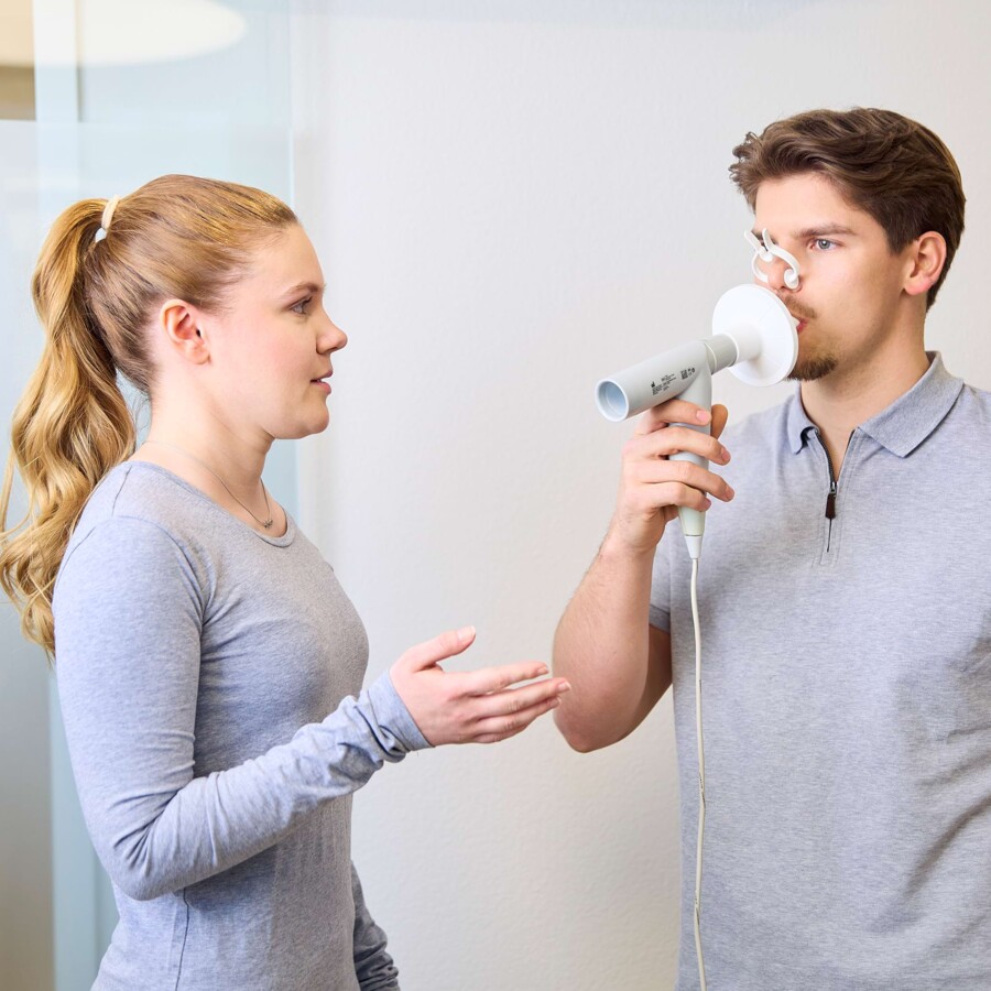 Eine medizinische Fachangestellte l&auml;sst einen Patienten in ein Messger&auml;t pusten.