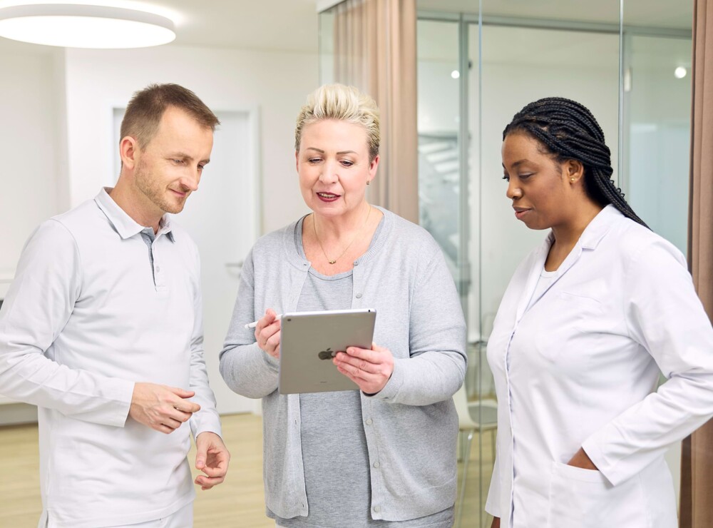 Zwei Mitarbeiterinnen und ein Mitarbeiter unterhalten sich und betrachten ein Tablet.