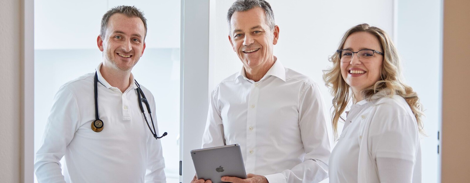 Zwei &Auml;rzte und eine &Auml;rztin unterhalten sich im Gang und drehen sich in einer Momentaufnahme zur Kamera um.