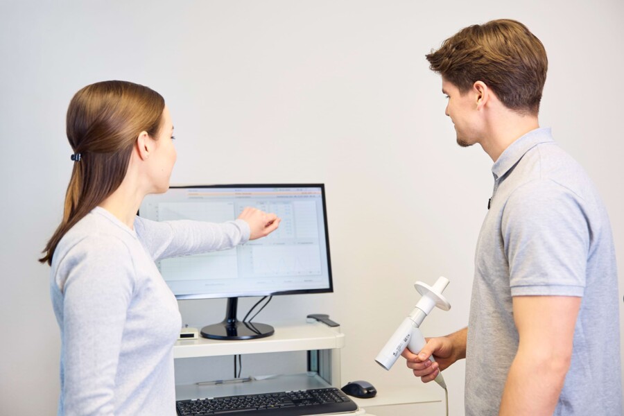 Einem Patienten werden auf einem Bildschirm die Ergebnisse seiner Messung gezeigt.