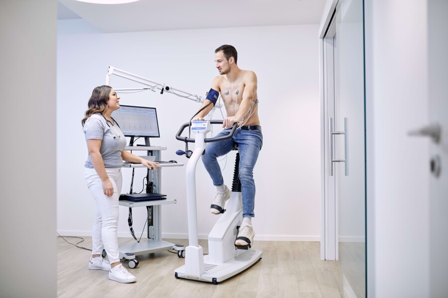 Eine Mitarbeiterin misst die Werte eines Patienten auf einem Pedal Trainer.