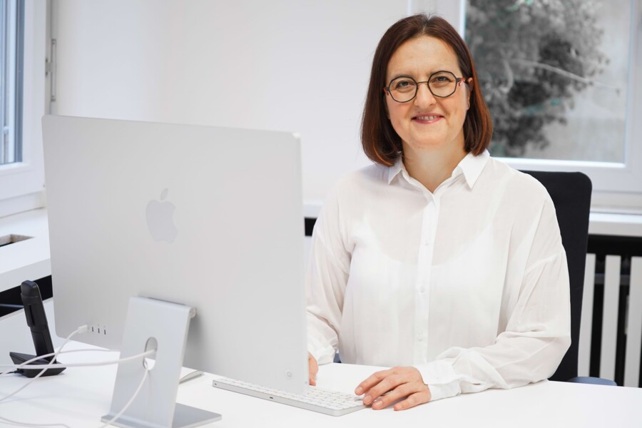 Helene Frank sitzt an ihrem Arbeitsplatz und l&auml;chelt zur Kamera.