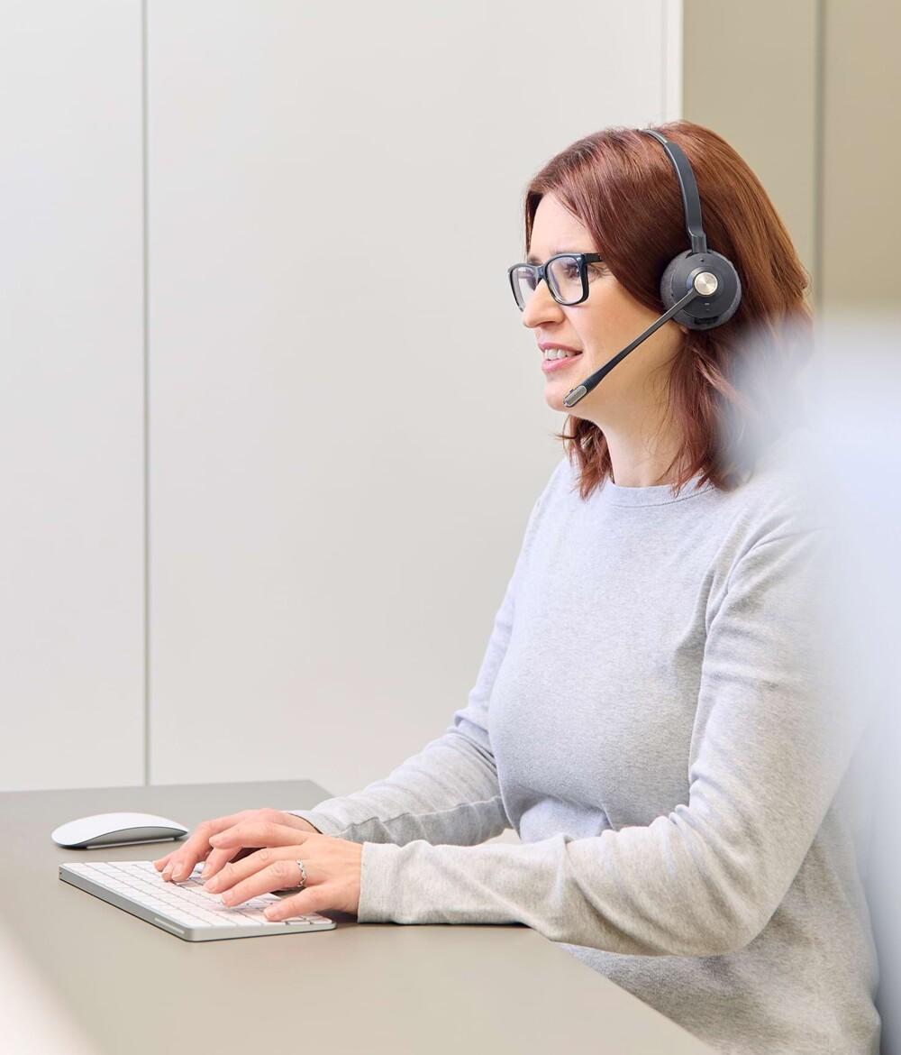 Eine Mitarbeiterin ist mit Headset am telefonieren und pr&uuml;ft etwas am PC.