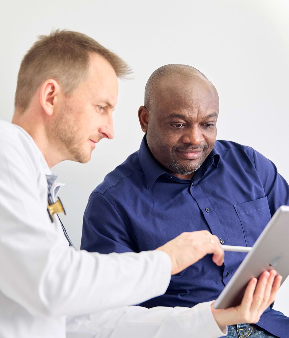 Ein Arzt erkl&auml;rt einem Patienten etwas auf einem Tablet.