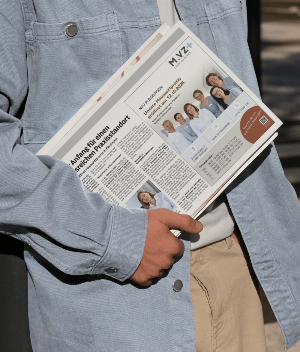 Ein Mann mit hellem Jeanshemd hat eine Zeitung in der Hand, auf der ein Zeitrungsartikel des MVZ-Buderer zu sehen ist.