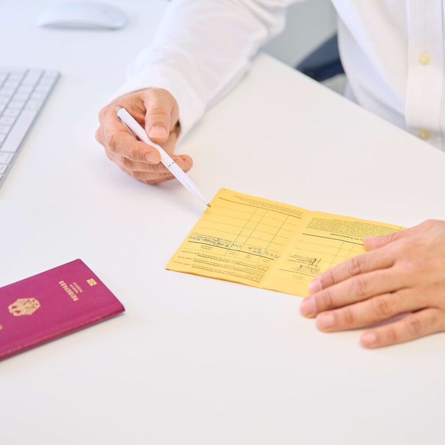 Ein Reise- und Impfpass liegen auf dem Schreibtisch eines Arztes, der den Impfschutz f&uuml;r anstehende Reisen checkt.