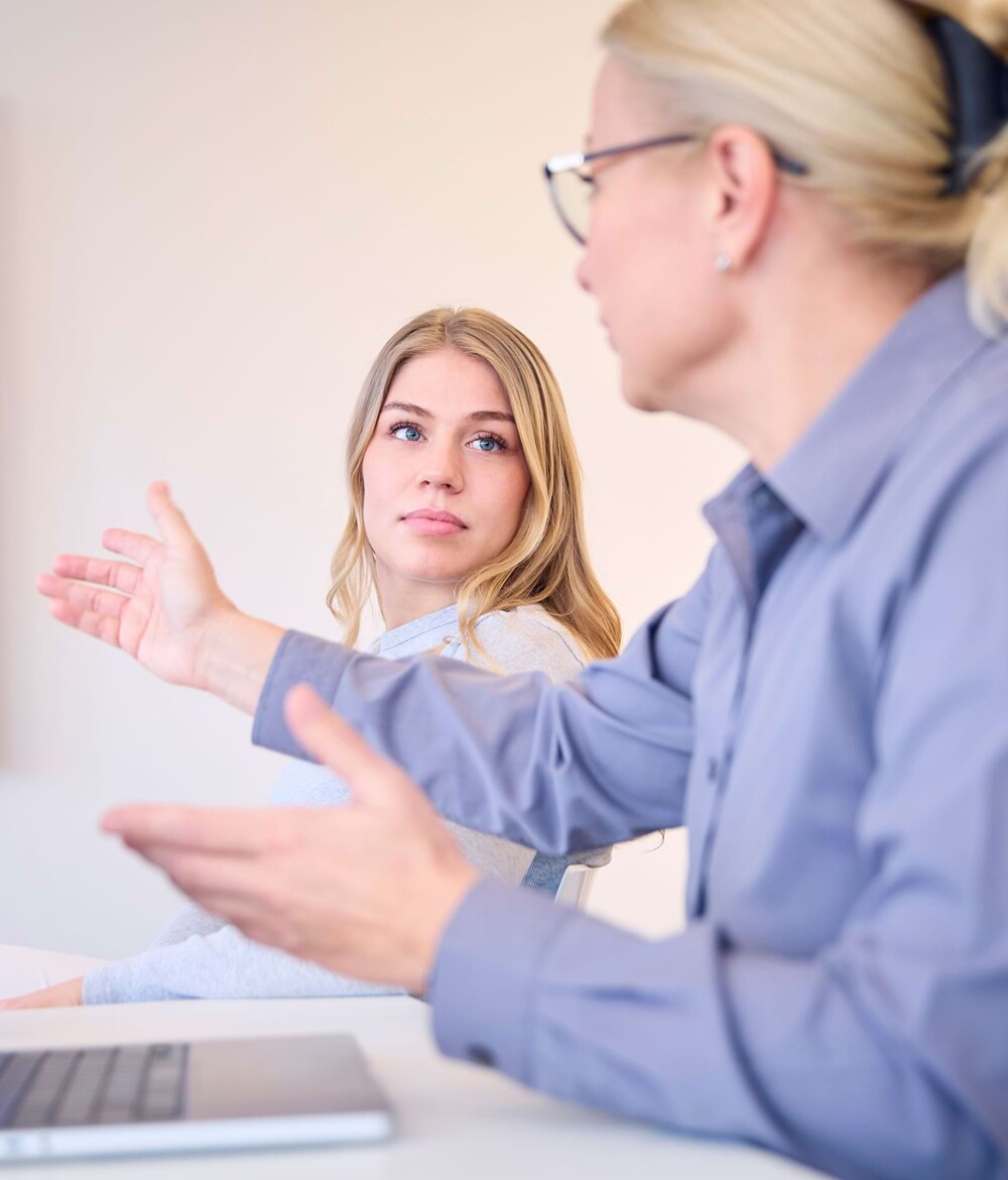 Eine Mitarbeiterin erkl&auml;rt einer j&uuml;ngeren Auszubildenden etwas.