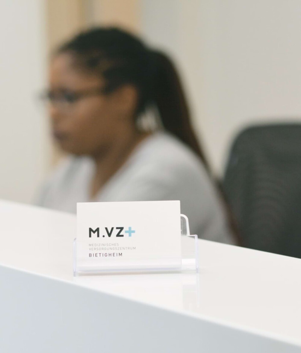 Nahaufnahme einer Visitenkarte des MVZ Team Buderer. Im Hintergrund ist die Rezeption zu sehen.