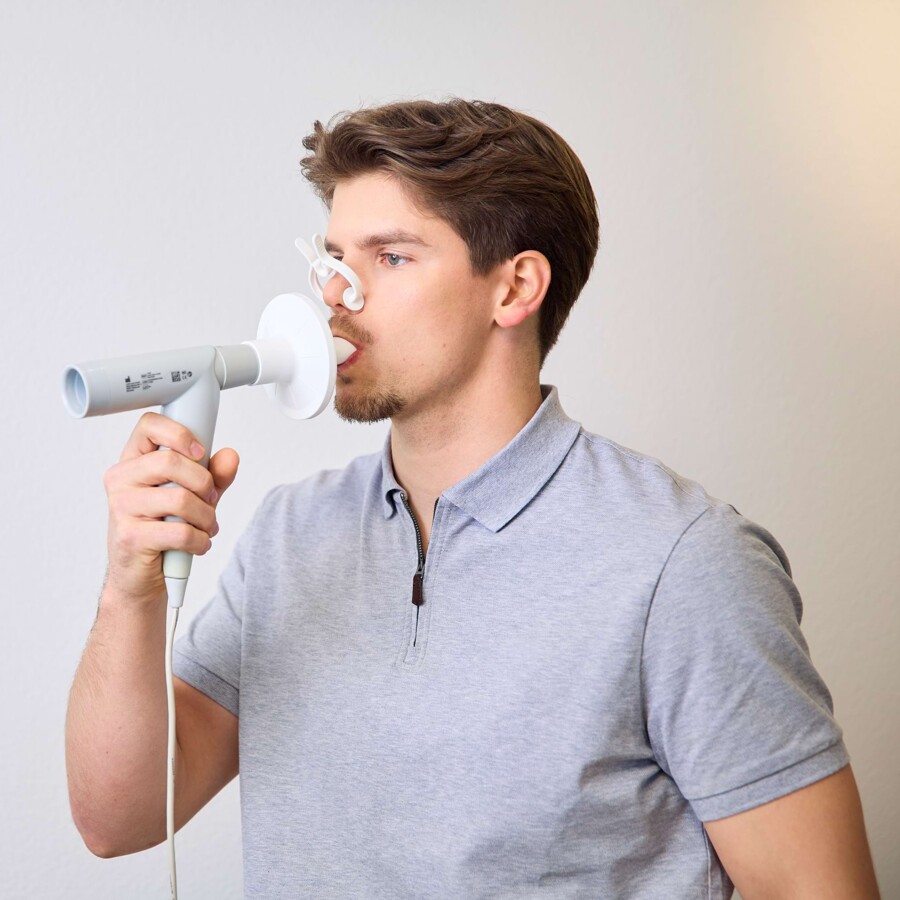 Ein junger Mann tr&auml;gt eine Nasenklemme und pustet in ein Messger&auml;t.