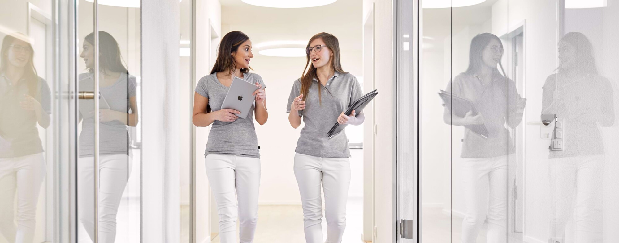 Zwei Mitarbeiterinnen unterhalten sich und laufen &uuml;ber einen Praxisflur.