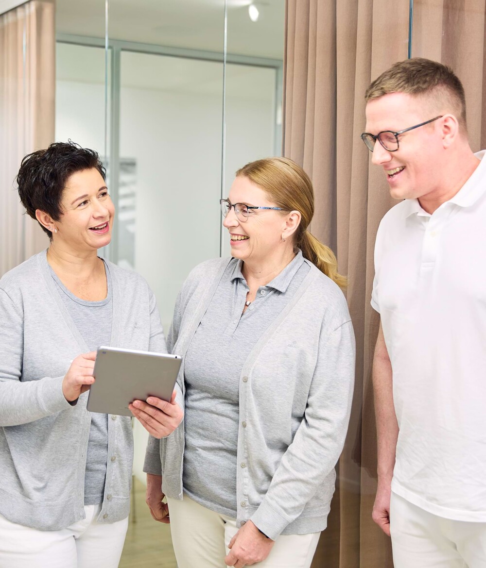 Drei Mitarbeiter:innen unterhalten sich auf dem Flur und lachen.