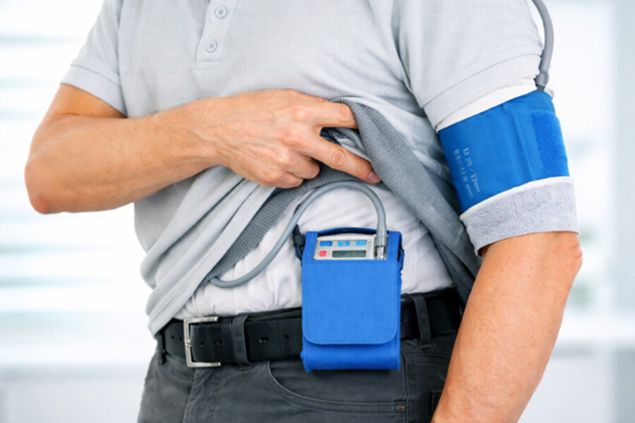 Ein Mann in schwarzer Jeans und grauem Polo tr&auml;gt an seinem G&uuml;rtel ein Ger&auml;t zur Langzeit EKG-Messung